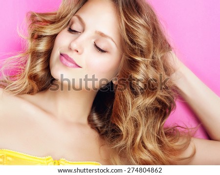 Portrait of a beautiful and gentle blonde girl in the studio on a pink background in a yellow dress, smiling