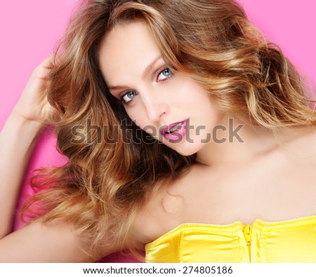 Portrait of a beautiful and gentle blonde girl in the studio on a pink background in a yellow dress