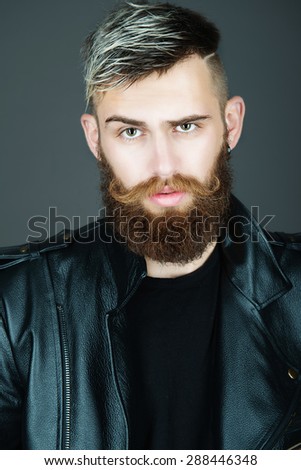 Portrait of an attractive bearded man in a studio in a black leather jacket on a dark background