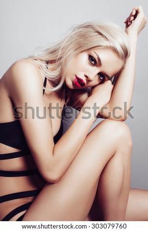 Portrait of a beautiful young blonde girl with long hair in a black bathing suit in the studio on a gray background, the concept of beauty
