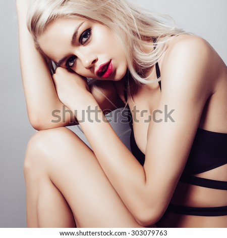 Portrait of a beautiful blonde girl with long hair in a black bathing suit in the studio on a gray background, the concept of beauty and health