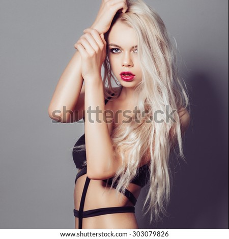 Portrait of a beautiful young blonde girl with long hair in a black bathing suit in the studio on a gray background, the concept of beauty and health