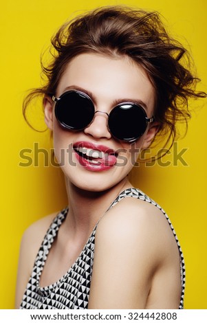 Portrait of a beautiful girl in round glasses on a yellow background in the studio
