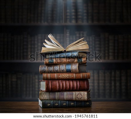 A stack of old books on table against background of bookshelf in library. Ancient books as a symbol of knowledge, history, memory and information. Conceptual background on education, literature topics