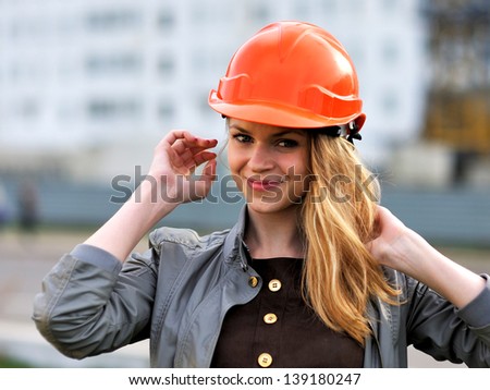 The young pleasant smiling girl with long hair costs against the building under construction