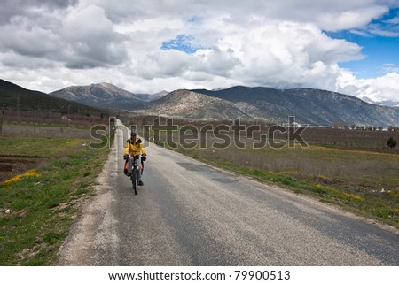 Cool girl traveling by bicycle in the countryside, with blue sky and clouds.