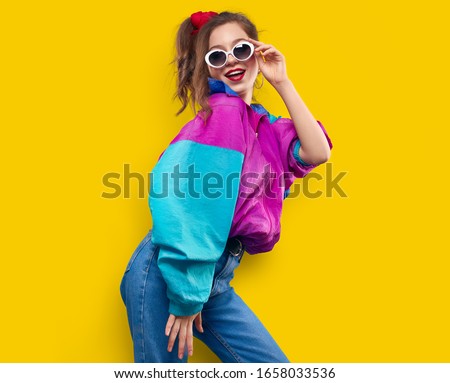 Cool teenager. Fashionable DJ girl in colorful trendy jacket and vintage retro sunglasses enjoys style of 80s - 90s vibes. Teenager Girl at disco party. Young fashion model on yellow color background.