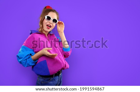 Cool teenager. Fashionable DJ girl in colorful trendy jacket and vintage retro sunglasses enjoys style of 80s - 90s vibes. Teenager Girl at disco party. Young fashion model on pink color background.