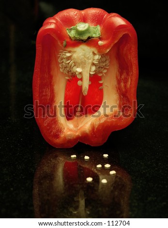 Wet red capsicum cut in half revealing inner pith/seeds.  some seeds on granite benchtop.
