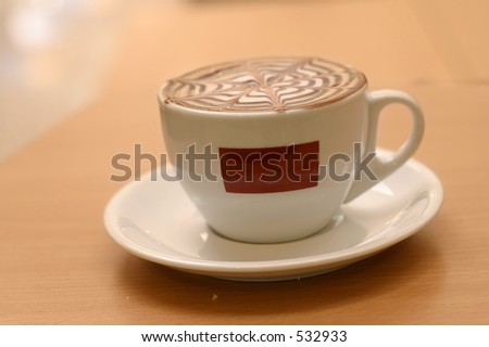 Mmmmm.  A delicious capuccino in a cafe - space for your logo or name as original was removed.  Focus on foreground cup . This image has a shallow dof.