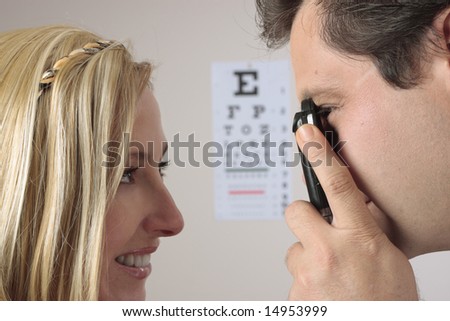 Closeup of a an optometrist eye doctor checking a female patient eyes.  Focus to man.