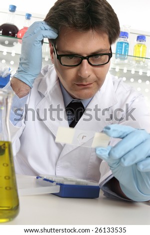 A scientist scratches his head whilst examining a microscope slide.