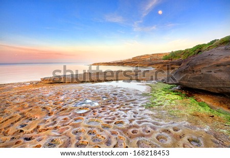 Sunrise at Botany Bay, La Perouse, Sydney Australia on a calm summers morning, the moon still shining overhead  of the strange moonscape crater like potholes in the rocks below.