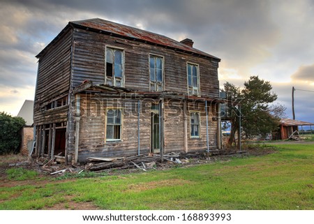 Abandoned dilapidated two storey late Victorian Georgian farm house with corrugated iron roof  and brick fireplace.  It once had an upper storey verandah with fancy wrought iron lattice work.