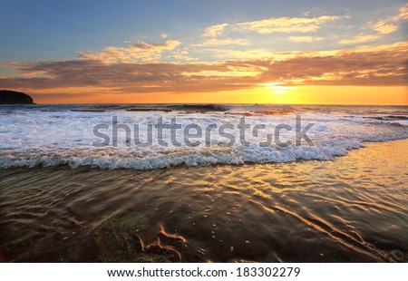 Waves crash and the water flows onto the rock shelf during high tide at sunrise.