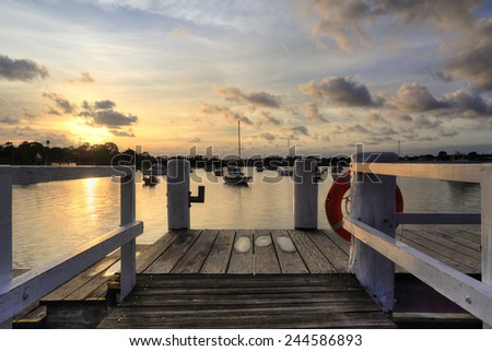 The afternoon golden sun sets over Iron Cove , views from the timber wharf  lead the eye through to moored boated bobbing on the waters from Liechhardt Park, NSW, Australia.