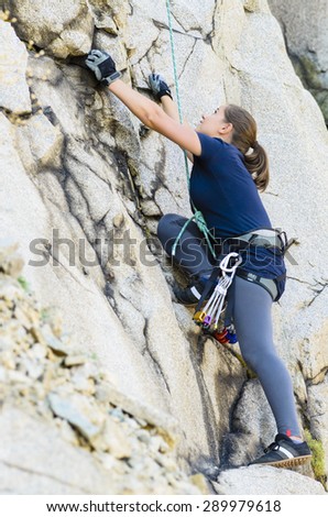 A young woman climbing on a granite face equipped with climbing gear