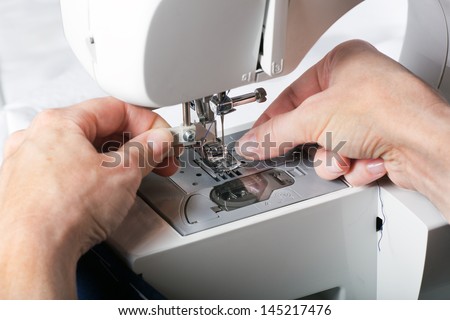 Hand threading needle into sewing needle. For concepts such as fashion and design, work and industrial.