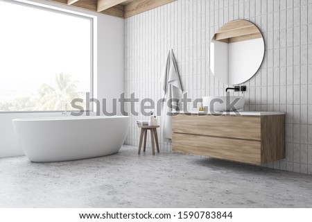 Corner of hotel bathroom with white and tiled walls, concrete floor, comfortable bathtub standing under window and sink on wooden countertop with round mirror. 3d rendering