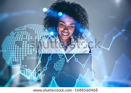 Cheerful young African American woman trader using laptop in blurry office with double exposure of blurry financial chart and planet hologram. Concept of stock market and technology. Toned image
