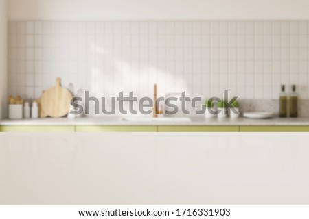 White table for your product standing in blurry kitchen with white tiled walls and green countertops with built in sink. 3d rendering mock up