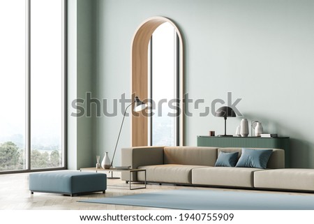 Modern living room interior with arch, mint color on wall and panoramic windows, hills view. Beige sofa with blue cushions, coffee table, light green chest of drawers. Parquet floor. 3D rendering