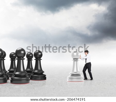 Young businessman moving a pawn on the grey desk under the silver sky.