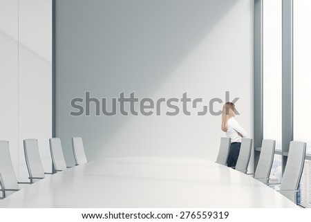 Side view of the young beautiful lady who is looking out the panoramic window in an office. Conference room in a modern office of a consulting company.