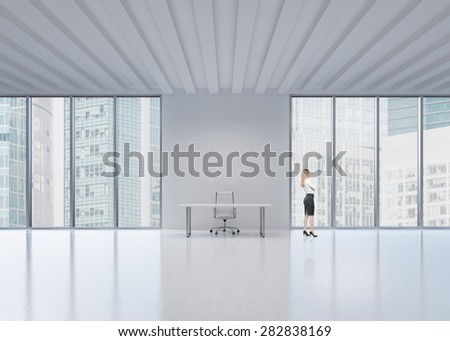 Side view of the blonde employee who looks out the window in New York\'s panoramic office. A concept of the modern workplace.