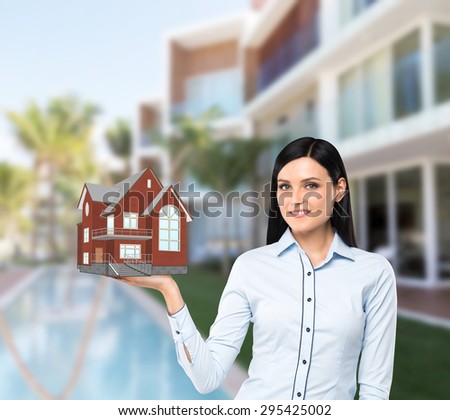 Beautiful brunette property agent presents a new house for sale. Luxury villa in blur as a background.