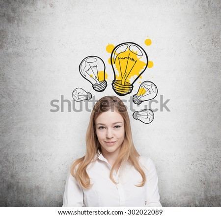 Charming young lady creates new business ideas. Drawn yellow light bulbs on the concrete wall.