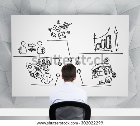 Rear view of a businessman on the workplace who is looking at the charts, pie chart, business icons which are drawn on the whiteboard. A concept of about business development strategy.