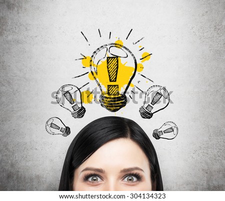 A head of young brunette lady who is thinking about new business ideas. A light bulb are drawn on the concrete wall.