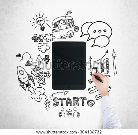 A tablet, digital device is surrounded by drawn business icons. A hand is drawing a bar chart. Concrete background.