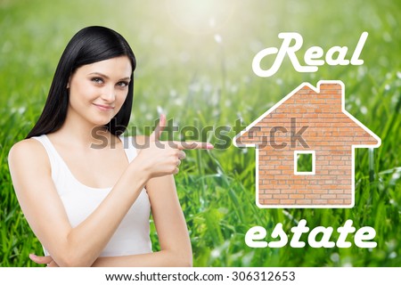 Brunette real estate agent is pointing out the house for sale. Green grass background.