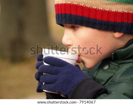 young boy with hat and gloves drinking hot chocolate outdoors