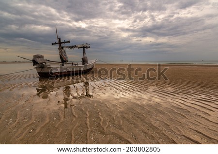 And old fishing boat beached on the sand during low tide with gloomy clouds overhead