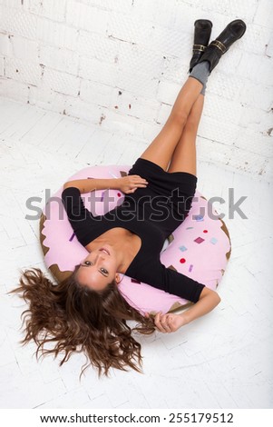 Playful girl lies on a big donut and smiling White brick wall, not isolated