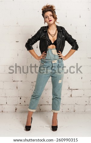 Serious young woman in the style of oldschool in a black jacket. White brick wall not isolated