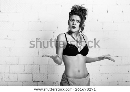 Unhappy young woman in coveralls plants hands. White brick wall not isolated