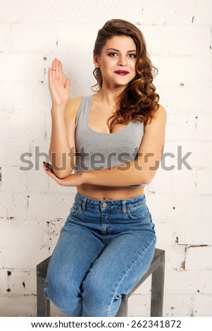 Beautiful young woman lifts his right hand up in school. White brick wall not isolated