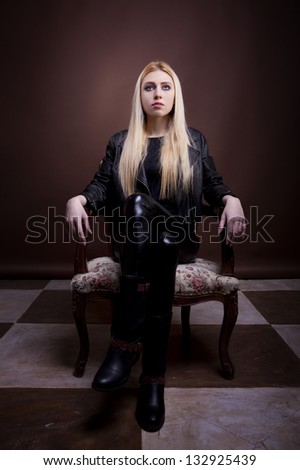 Gorgeous rock girl sitting on a vintage chair full body studio shot