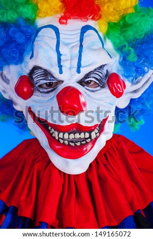 Scary clown person in clown mask on blue background studio shot