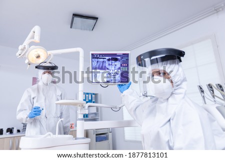 Patient pov of doctor pointing at stomatological monitor with dental x-ray. Stomatology specialist wearing protective suit against infection with coronavirus pointing at radiography. Foto stock © 