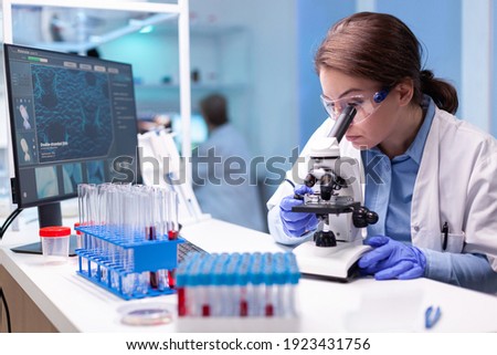 Scientist looking into microscope in virus research laboratory with pharmacy development equipment. Woman working on science vaccine chemistry experiment in modern lab, analyzing pharmaceutical work Foto stock © 
