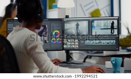 African video editor working with footage and sound, editing new project cutting film montage sitting in modern agency office. Woman using computer processing movie in post production software