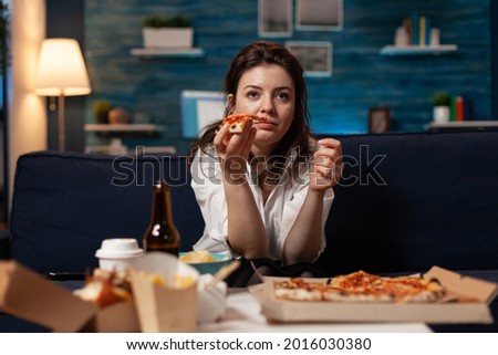 Portrait of woman watching comedy movie eating tasty delivery pizza slice relaxing on sofa in living room at night. Caucasian female enjoying takeaway food home delivered. Fastfood meal order Stock fotó © 