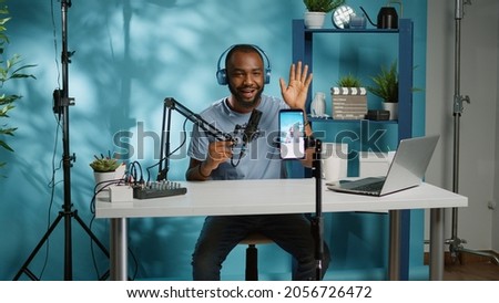 African american vlogger using smartphone to film podcast in studio. Black blogger with mobile phone, microphone and headphones filming video for social media broadcasting career.