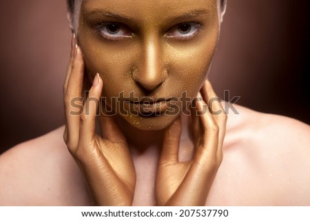 Woman with art fashion make up on face. Brown background. Gold skin type make up