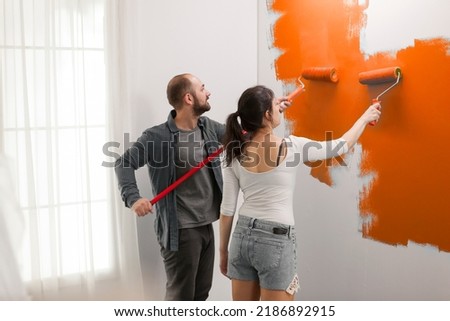 Confident couple using orange color paint on walls to redecorate apartment room during interior design renovation. Doing housework redecoration with painting tools, ladder and diy equipment. Imagine de stoc © 